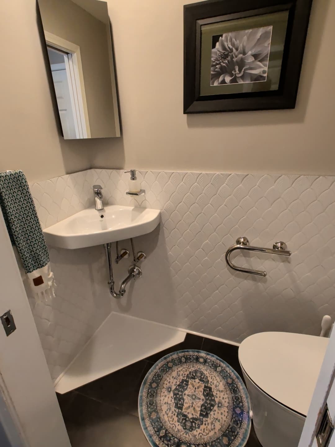 Small bathroom renovation with modern toilet, corner sink, white decorative wall tile, and dark tile flooring