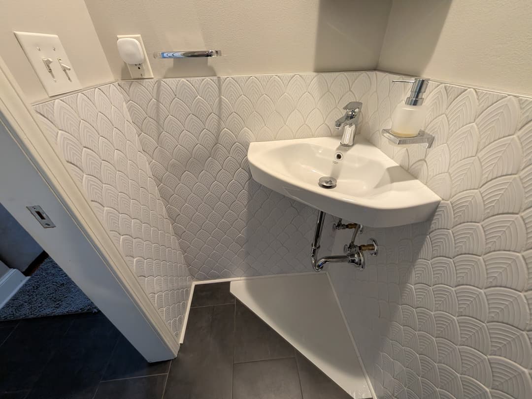 Corner sink and tile detail in a remodeled half bathroom with dark floor tile and clean modern finishes