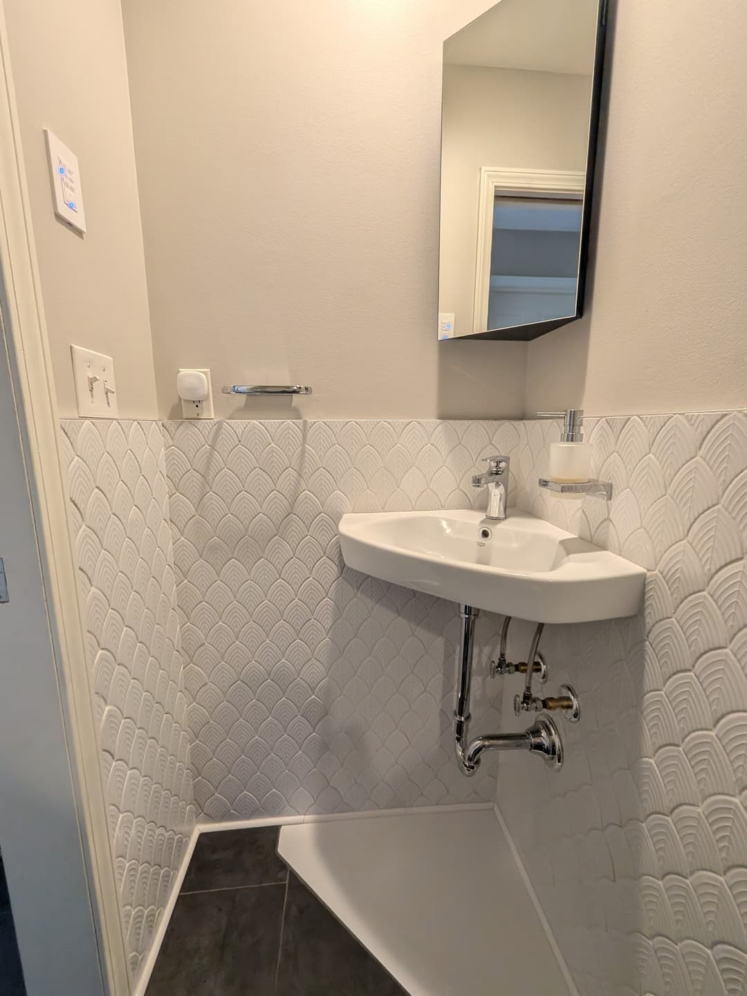 Top view of renovated powder room with modern toilet, textured white tile walls, and dark porcelain floor tile